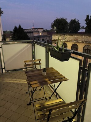 A terrace with a wooden table and chairs, a hanging planter with a plant, and a view of buildings in the background. - ShaMic Apartment | Comfort moderno a Milano • M1 Rossa a 350 m (Milano)