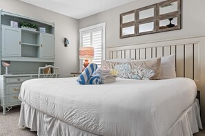 A bedroom with a large bed, a bedside table with a lamp, a dresser, and a mirror. - Na Da Shell OIB- Canal Home, Private Pool! (Ocean Isle Beach)