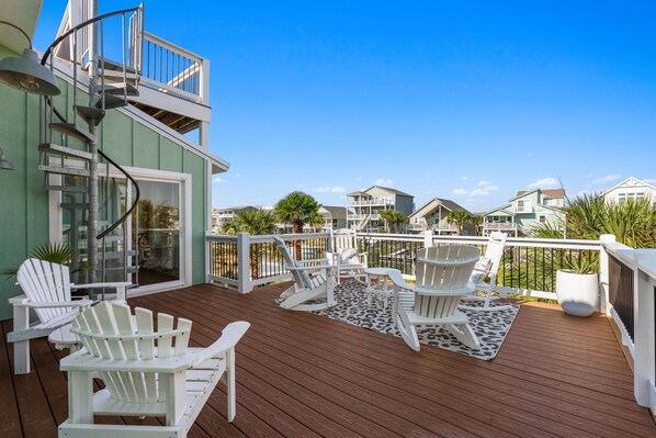 Una terraza de madera con sillas Adirondack blancas y una escalera espiral.