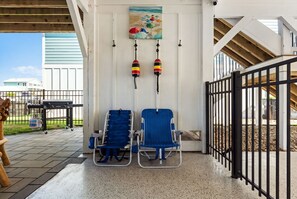 A covered outdoor seating area with two blue chairs and a grill. - Na Da Shell OIB- Canal Home, Private Pool! (Ocean Isle Beach)