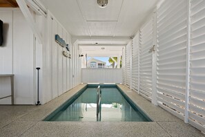 A pool area with a clear view of the outside, a metal ladder, and a door on the left. - Na Da Shell OIB- Canal Home, Private Pool! (Ocean Isle Beach)
