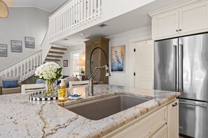 A kitchen with a marble countertop, stainless steel appliances, and a view of a staircase leading to another level. - Na Da Shell OIB- Canal Home, Private Pool! (Ocean Isle Beach)