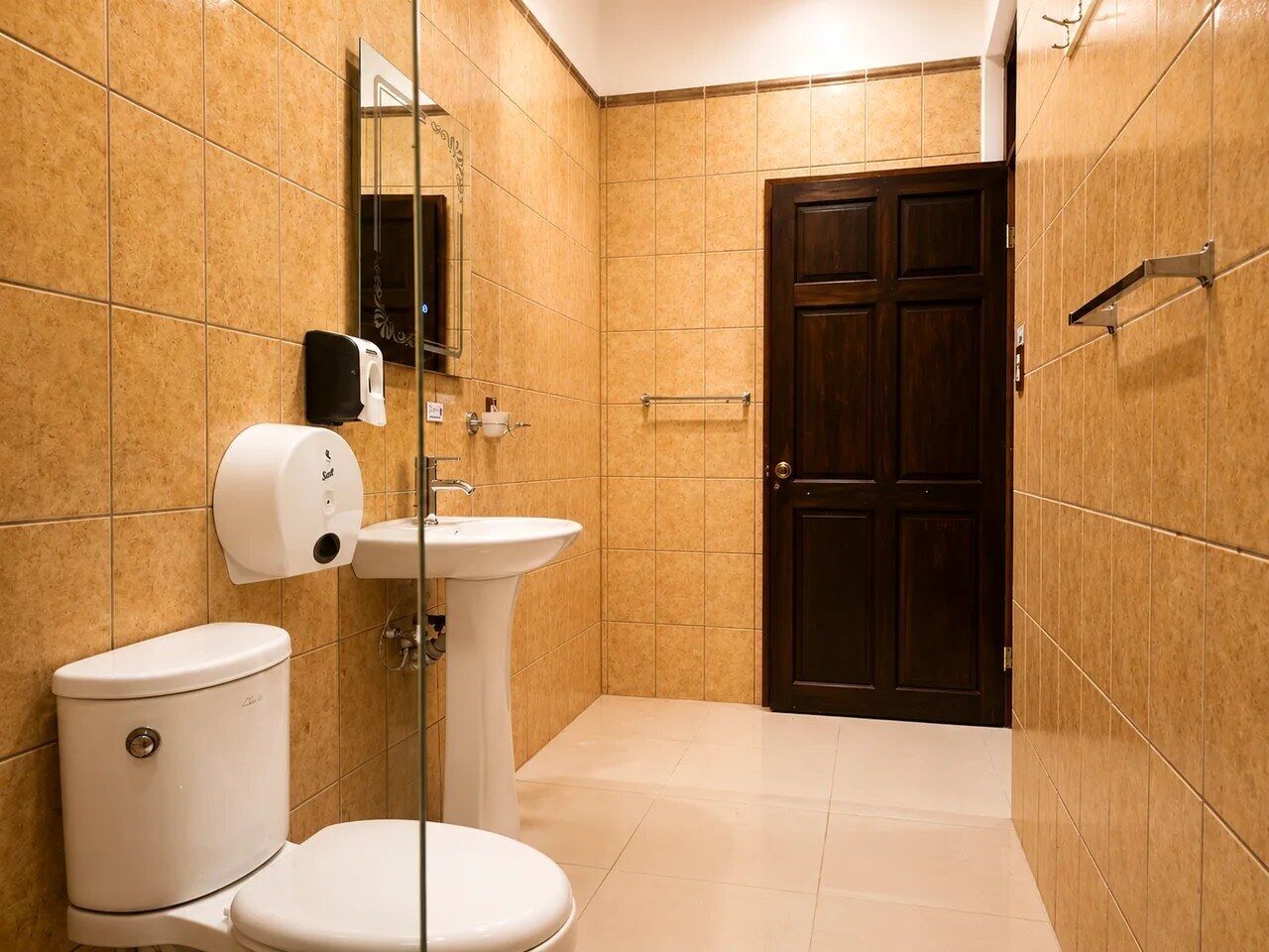 Un baño con inodoro, lavamanos y una puerta de madera oscura.