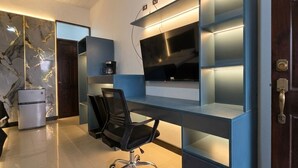 A modern office space with a built-in desk, a chair, a flat-screen TV, and a coffee machine. - Congos Hotel (Aguas Zarcas)