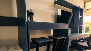 A modern office space with a desk, two chairs, a coffee machine, and a shelf with folded towels. - Congos Hotel (Aguas Zarcas)