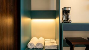 A hotel room with a teal-colored shelf holding rolled towels, a coffee maker on a table, and a wooden door. - Congos Hotel (Aguas Zarcas)