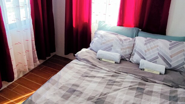 Un letto con una coperta a quadri, cuscini e un asciugamano arrotolato.