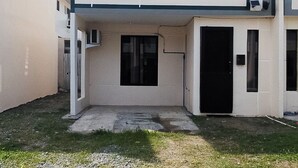 Un edificio a due piani con tetto piatto, un piccolo giardino antistante e una porta nera.