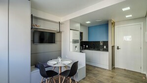 A modern kitchen with a built-in oven, a microwave, and a coffee machine. There is a dining area with a table and chairs, and a television mounted on the wall. - Modern Studio in Poa, Building With gym Mcp0213 (Porto Alegre)
