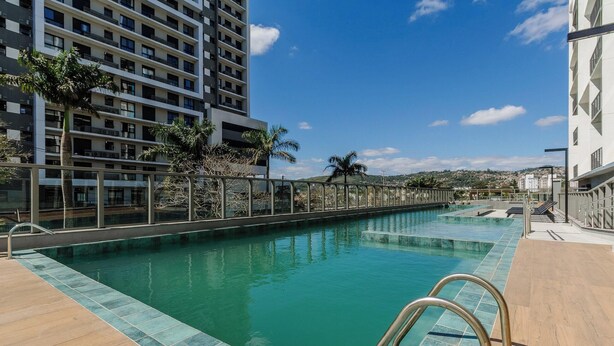 A swimming pool with a clear blue water surface, surrounded by a wooden deck and metal railings. - Modern Studio in Poa, Building With gym Mcp0213 (Porto Alegre)