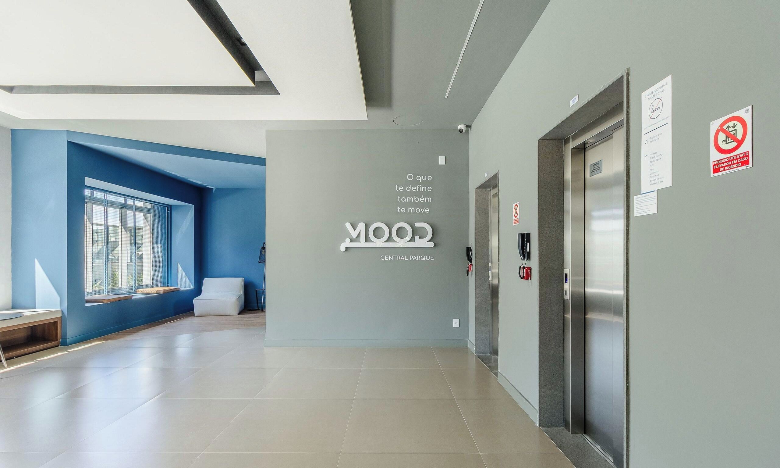 Un couloir moderne avec un mur d’accent bleu, un panneau indiquant l’entrée d’un parc, et un ascenseur.