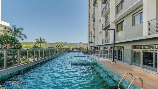 A swimming pool with a view of a modern building and a distant landscape. - Studio w/ Pool Near PUC Mcp0403 (Porto Alegre)
