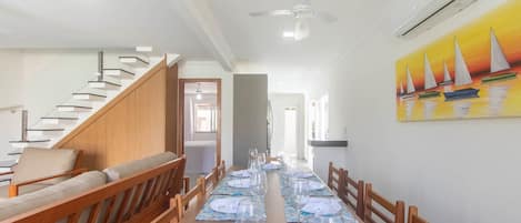 A dining area with a long table set for a meal, wooden chairs, a staircase, and a painting on the wall.