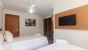 Ein Hotelzimmer mit zwei Betten, einem Deckenventilator, einem Gemälde, einem Fernseher und einem Kleiderschrank.