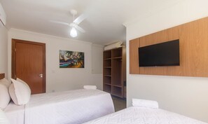 Ein Hotelzimmer mit zwei Betten, einem Deckenventilator, einem Gemälde, einem Fernseher und einem Kleiderschrank.