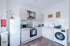 Una cocina moderna con armarios blancos, un microondas, un tostador, un lavamanos y una lavadora.