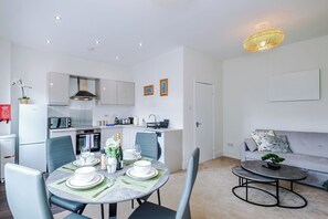 Un espacio habitable compacto con comedor, kitchenette y zona de estar con sofá y mesa de centro.
