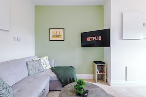 Una sala de estar moderna con un sofá gris, una mesita de centro, un cuadro en la pared y un televisor mostrando 'NETFLIX'.