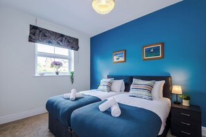 A bedroom with two beds, a window with a view, and a nightstand with a lamp.
