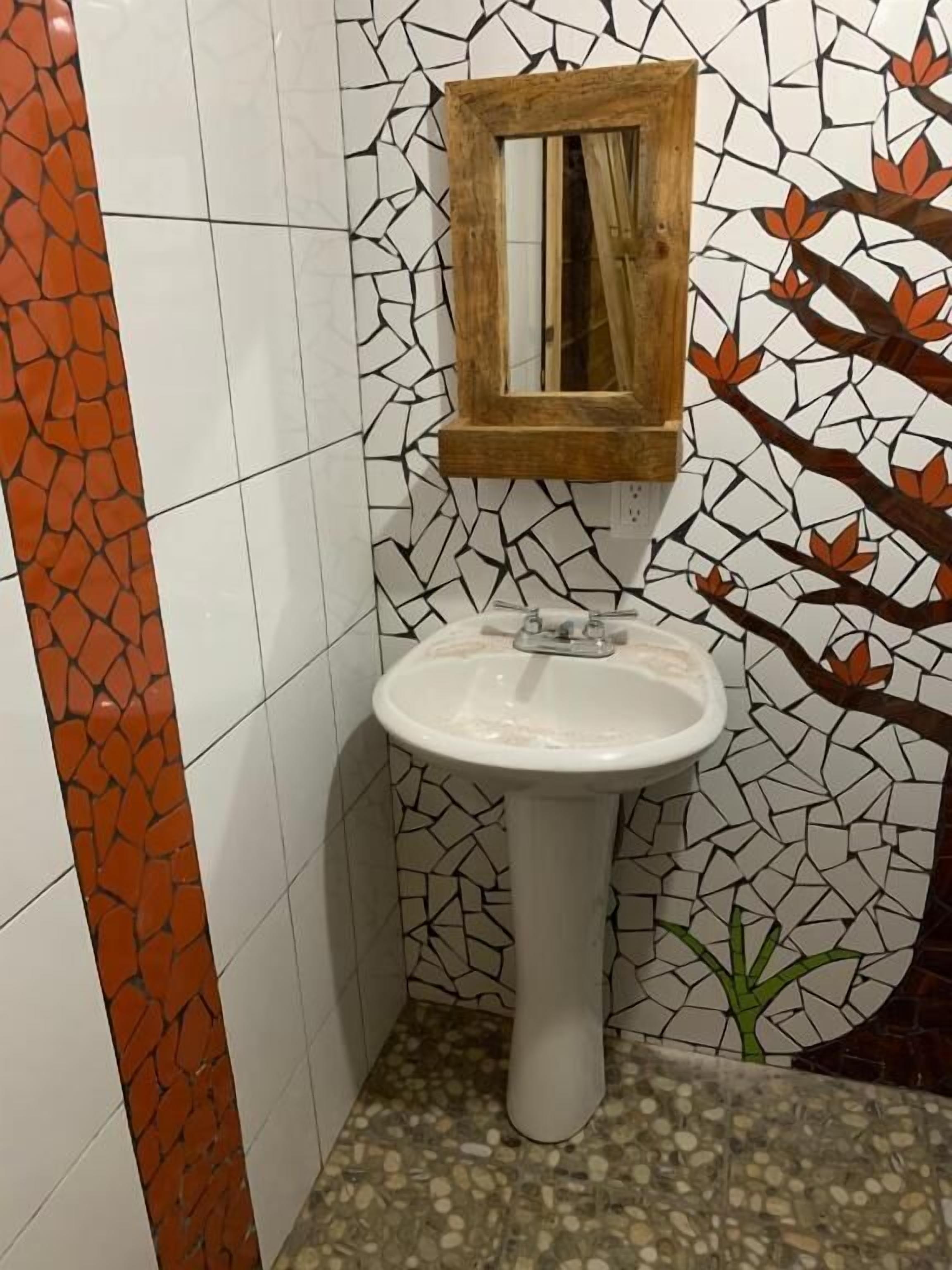 A bathroom with a white sink, a wooden-framed mirror, and a mosaic wall with a tree design.
