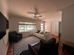 A living room with a ceiling fan, a large window with blinds, a patterned rug, a sofa, and a black leather chair. - Quiet Denver Home Near DU, Cherry Creek, Wash Park & Wellshire Golf (Denver)