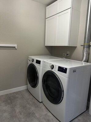 A laundry room with two front-loading washing machines, a white cabinet above, and a vent pipe to the right. - Quiet Denver Home Near DU, Cherry Creek, Wash Park & Wellshire Golf (Denver)
