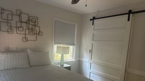 Un dormitorio con cama, ventana con persianas, mesita de noche y puerta corredera.