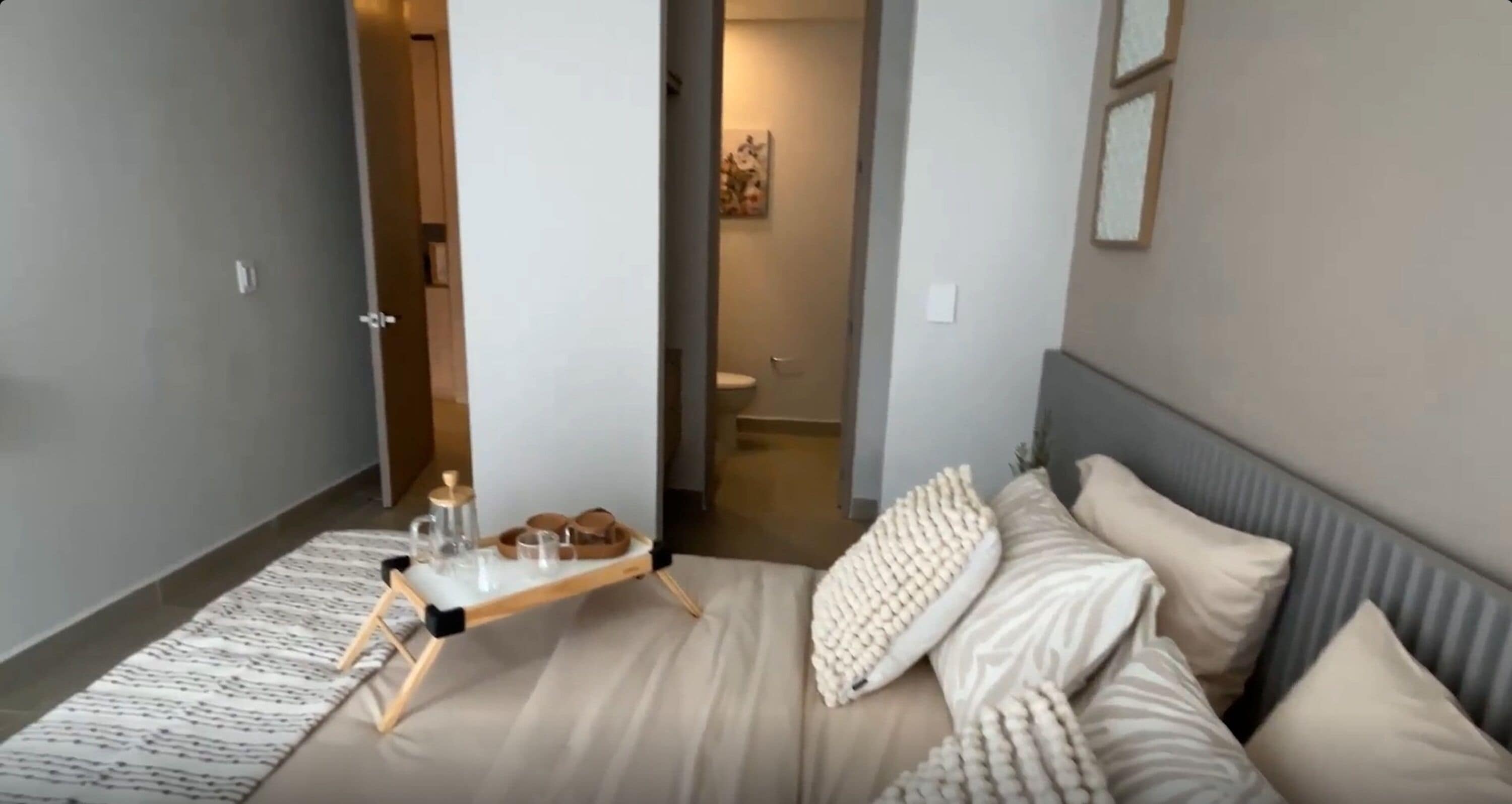 Une chambre à coucher moderne, avec un lit, des tables de chevet, une commode, une lampe de chevet et une salle de bain visible à travers une porte ouverte.
