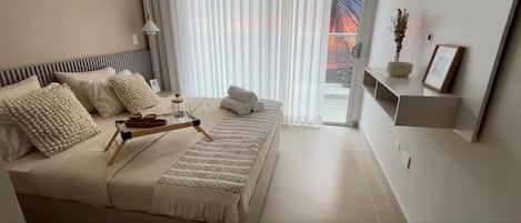 A modern bedroom with a bed, pillows, a bedside table with a tray, a potted plant, and a view of a bridge through the window.