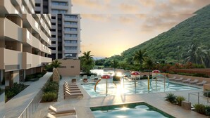 A hotel with a pool area, lounge chairs, and a view of a lush green hill. - Praia Suites by Avia Suites (Santa Marta)