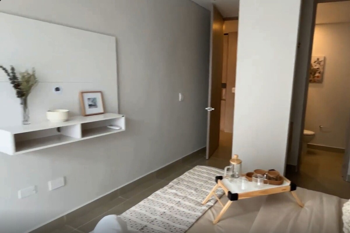Un salon moderne avec un canapé, une table basse sur laquelle est posé un plateau, et une étagère murale agrémentée d’objets décoratifs.