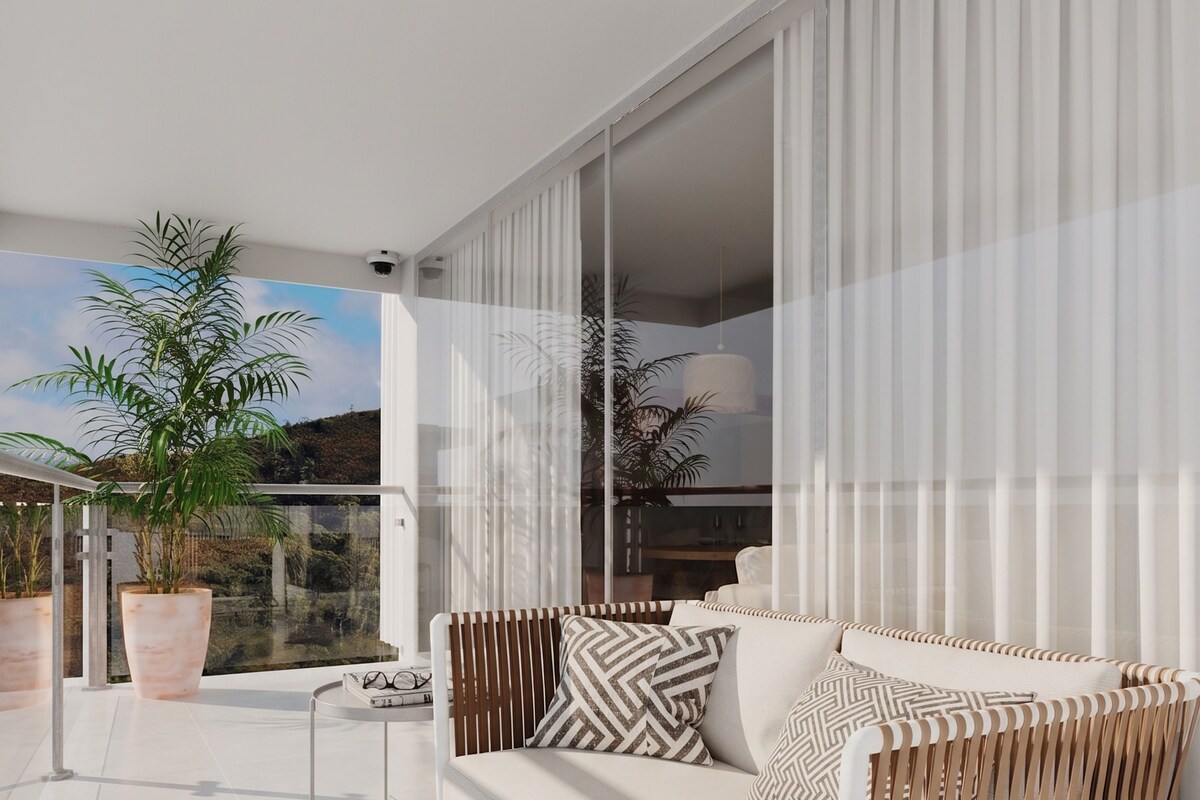 A modern outdoor seating area with a white sofa, patterned cushions, and a large potted plant.