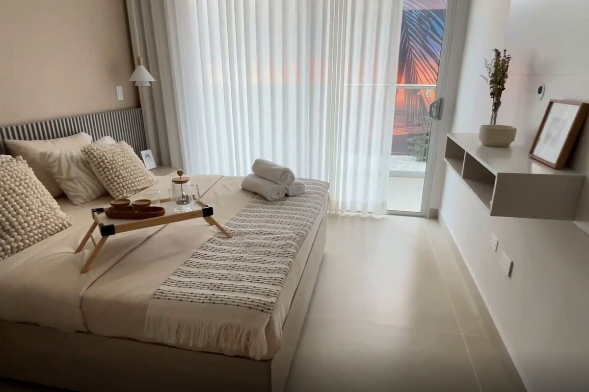 Ein modernes Schlafzimmer mit Bett, Kissen, Nachttisch mit Tablett, einer Topfpflanze und Blick auf eine Brücke durch das Fenster.