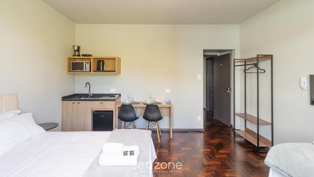 Quarto de hotel com cama, escrivaninha com micro-ondas, cafeteira, pia e closet espaçoso.