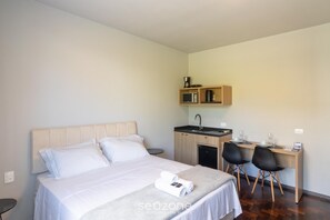 A hotel room with a bed, a desk with two chairs, a small kitchenette, and a single bedside table. - Studio in Condo w/ Parking in Blumenau Ola0004 (Blumenau)