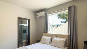 A bedroom with a bed, a window with curtains, an air conditioning unit, and a view of the outside. - Studio 750m From Vila Germanica Ola0005 (Blumenau)