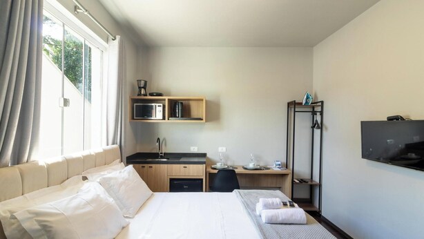 A hotel room with a bed, a desk, a microwave, a coffee maker, and a TV. - Studio 750m From Vila Germanica Ola0005 (Blumenau)