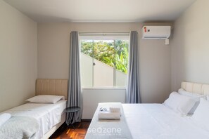 A hotel room with two beds, a window with curtains, an air conditioning unit, and a small table. - Studio w/ Garage, 750m fr/ Vila Germanica Ola0006 (Blumenau)