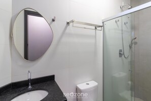 A bathroom with a round mirror, a sink, a toilet, and a glass-enclosed shower area. - Studio w/ Garage, 750m fr/ Vila Germanica Ola0006 (Blumenau)