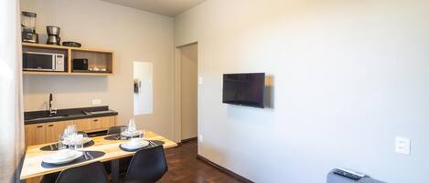 Un espacio habitable compacto con comedor, kitchenette y televisor montado en la pared.