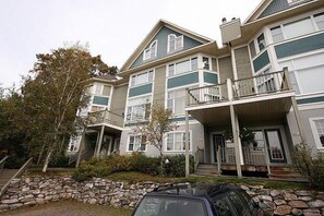 A multi-story residential building with a stone facade, balconies, and a car parked in the driveway. - L'Après-Ski Mont-Tremblant (Mont-Tremblant)