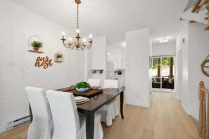 A dining area with a chandelier, white chairs, and a table set for four. - L'Après-Ski Mont-Tremblant (Mont-Tremblant)