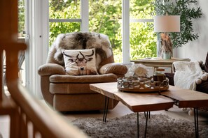 A cozy living room with a plush armchair, a small table with a candle, and a view of greenery outside. - L'Après-Ski Mont-Tremblant (Mont-Tremblant)