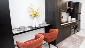 A modern kitchen with dark cabinetry, a black countertop, and two orange chairs. - Executive Studio at LoxwoodHouse, East Legon (Accra)
