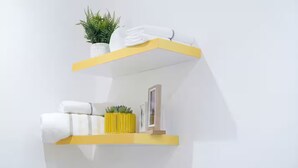 Two white shelves with yellow edges, one holding a potted plant and folded towels, the other with a framed picture and a small yellow vase. - Executive Studio at LoxwoodHouse, East Legon (Accra)