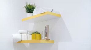 Two white shelves with yellow edges, one holding a potted plant and folded towels, the other with a framed picture and a small yellow vase. - Executive Studio at LoxwoodHouse, East Legon (Accra)