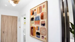 A hallway with a wooden door, a wall-mounted abstract painting, and a plant on a shelf. - Executive Studio at LoxwoodHouse, East Legon (Accra)