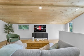 Una sala de estar moderna con techo de madera, televisor de pantalla plana, una silla verde, un sofá gris y una mesa de centro de madera.