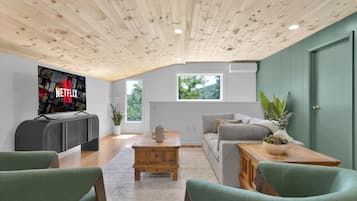 Una sala de estar moderna con techo de madera, un televisor de pantalla plana grande, un sofá gris y una mesa de centro.