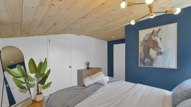 Un dormitorio con cama, mesitas de noche, espejo, planta y un cuadro en la pared.